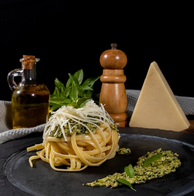 Pasta spaghetti with pesto sauce and fresh basil leaves in black stone dish on wooden background.