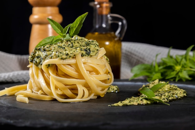 Pasta spaghetti with pesto sauce and fresh basil leaves in black stone dish on wooden background.