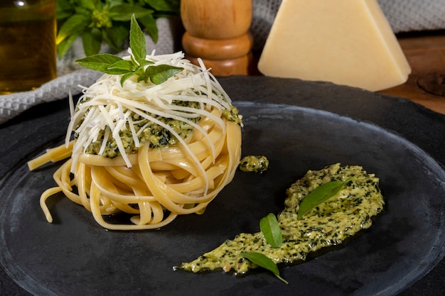 Pasta spaghetti with pesto sauce and fresh basil leaves in black stone dish on wooden background.