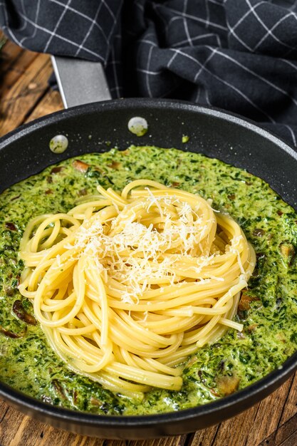 鍋にペストソースと新鮮なほうれん草とパルメザンチーズを添えたパスタスパゲッティ。木製の背景。上面図。