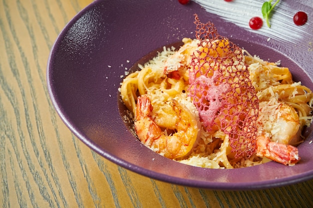 Pasta spaghetti with shrimps and parmesan cheese. Pasta with seafood in a violet bowl against a wooden surface. Italian cuisine