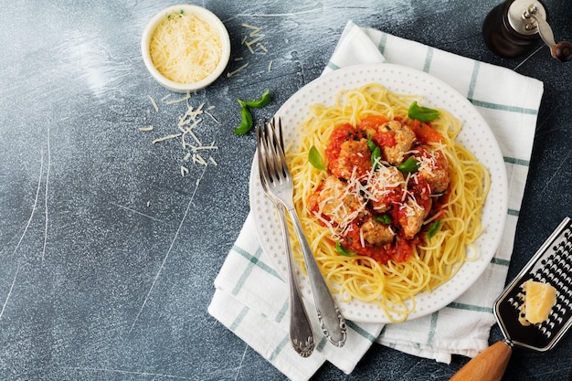 Spaghetti di pasta con salsa di pomodoro, parmigiano, basilico e polpette di carne sul piatto in ceramica bianca su cemento grigio o sfondo di pietra