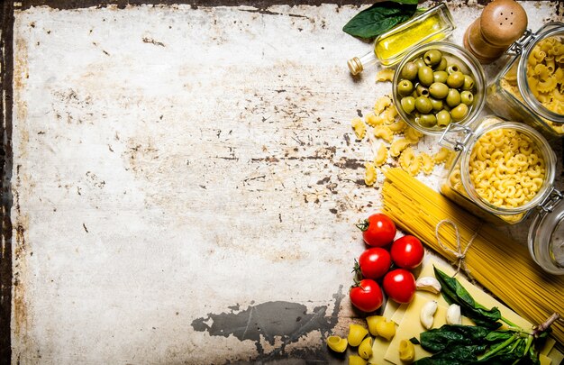 Pasta tafel. Veel verschillende pasta's, olijven, tomaten, olie en kruiden. Op rustieke tafel. Vrije ruimte voor tekst. Bovenaanzicht