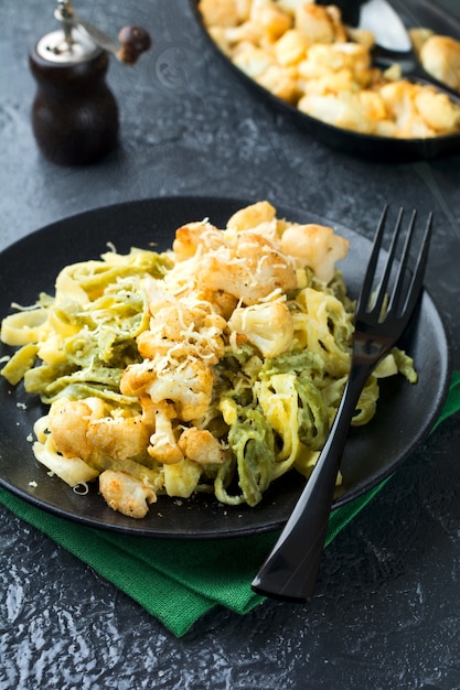 Foto tagliatelle di pasta in salsa cremosa con cavolfiore al forno in un piatto su uno sfondo scuro.