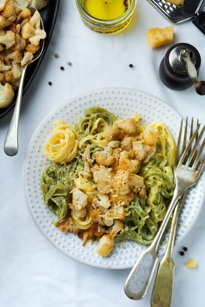 Tagliatelle di pasta in salsa cremosa con cavolfiore al forno in un piatto su una superficie leggera