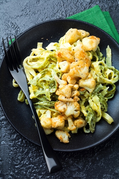 Pasta Tagliatelle in romige saus met gebakken bloemkool in een bord op een donkere ondergrond. Selectieve aandacht. Bovenaanzicht.