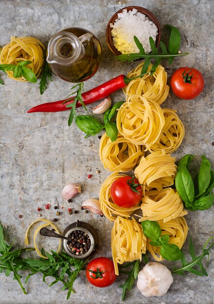 Pasta Tagliatelle nest and ingredients for cooking (tomatoes, garlic, basil, chili). Top view