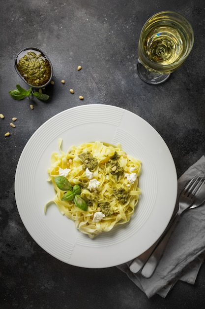 Pasta tagliatelle with pesto, pine nuts, white wine glass on dark. Delicious Mediterranean lunch.