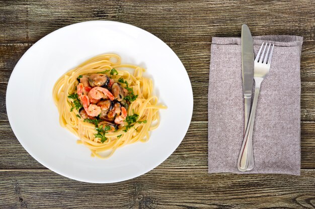 Pasta tagliatelle with seafood and cream sauce on a white plate on a wooden table. Top view.