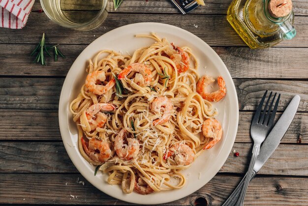 Foto tagliatelle di pasta con gamberi in salsa cremosa su piatto bianco su sfondo rustico in legno vista dall'alto