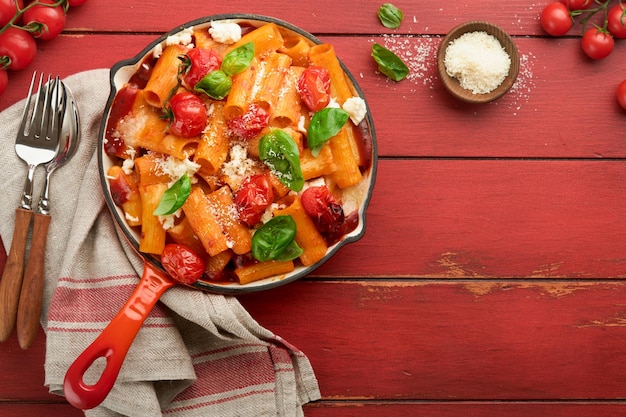 Pasta Tortiglioni with tomato sauce baked cherry tomatoes mozzarella and parmesan cheese basil on old red rustic table Traditional Italian cuisine Example Italian food for article Top view