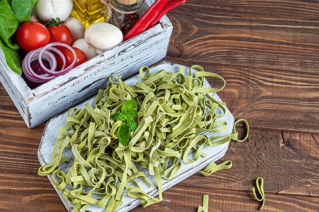 Pasta, vegetables, herbs and spices, olive oil, ingredients for Italian cuisine on a wooden brown background.