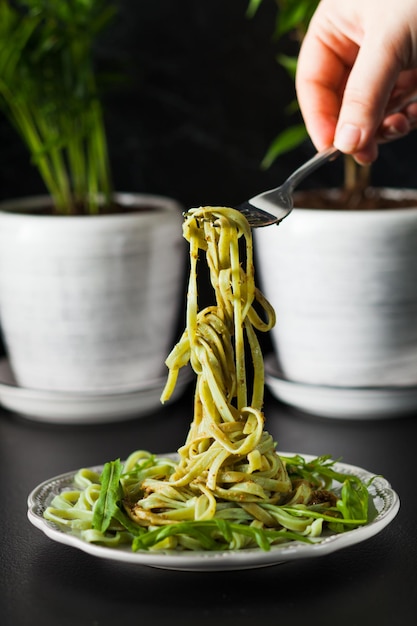 Pasta with arugula and pesto on the plate. Woman's hand hold the fork with spinach tagliatelle