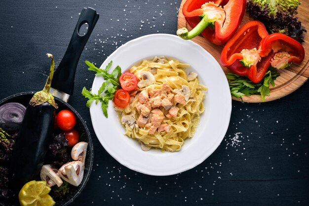 Pasta with bacon cherry tomatoes olives and mushrooms with parmesan cheese Italian food On a black wooden surface Free space for your text Top view