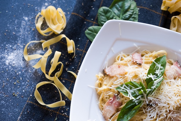 Pasta with bacon, cream, basil, parmesan, garlic, egg (yolk) on white plate