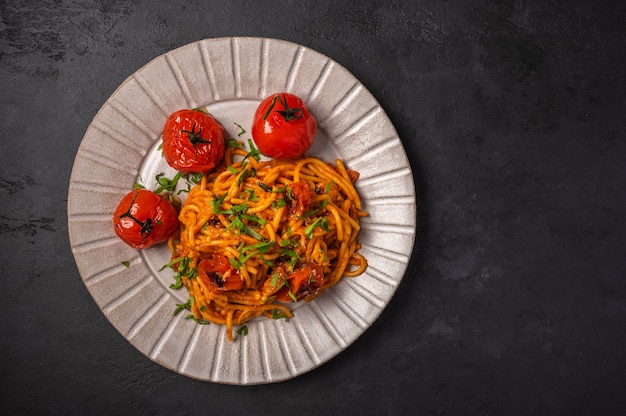 Pasta with baked cherry tomatoes, cheese and parsley on a dark textured background, top view, copy