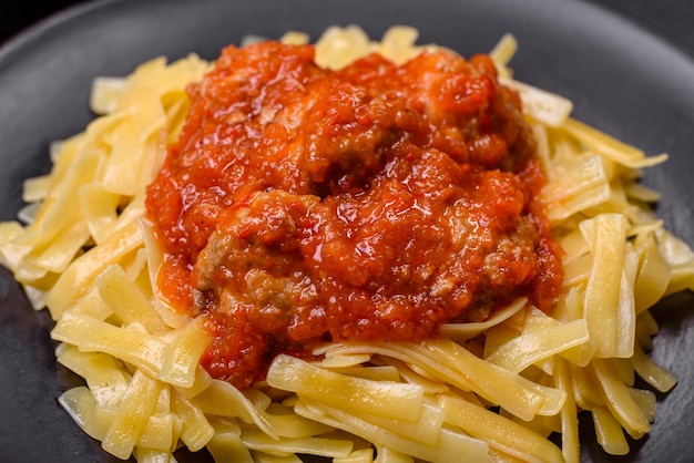 Pasta with beef meatballs in tomato sauce with spices and herbs on a dark background