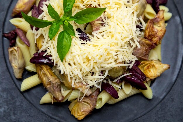 Pasta with black olives, Parmesan cheese, artichoke hearts, topped with fresh basil leaves.