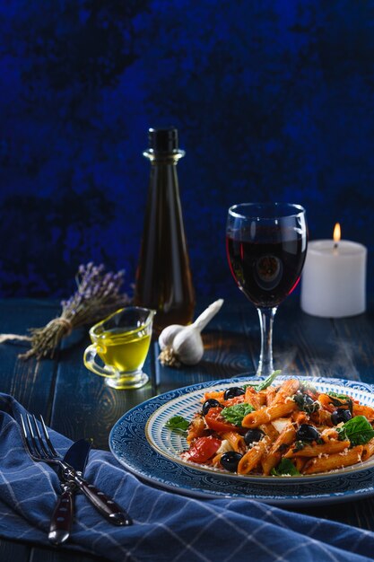 Pasta with cherry tomatoes, mozzarella and spinach olives, wine and oil on a wooden table. Rustic style.