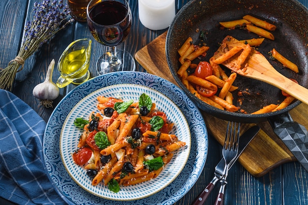 Pasta with cherry tomatoes, mozzarella and spinach olives, wine and oil on a wooden table. Rustic style.