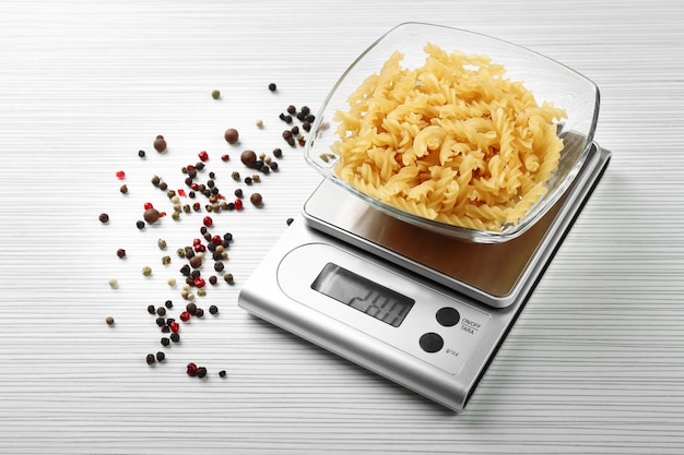 Pasta with digital kitchen scales on wooden background