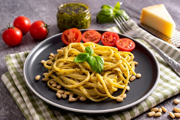 Pasta with fresh homemade pesto sauce on grey concrete background. Traditional italian spaghetti with food Ingredients pesto sauÃÂÃÂe, tomato, parmesan cheese, pine nuts and fresh basil leaves