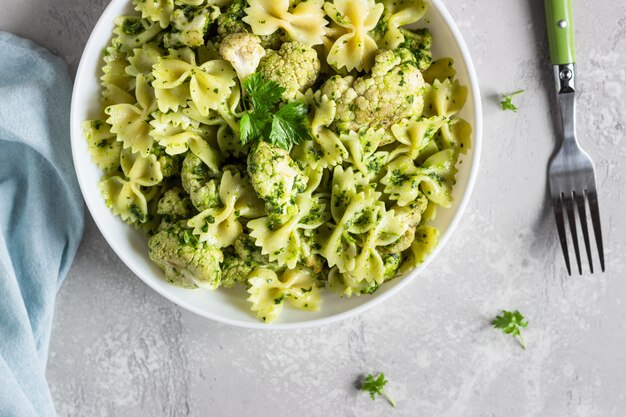 Pasta with green sauce and roaster cauliflower on a white plate. Copy space.