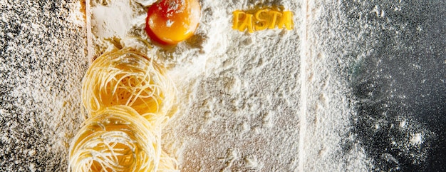 Pasta with ingredients - flour, eggs and different tools for cooking on black table. Free space for text . Top view.