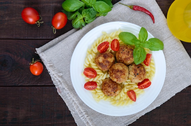 Pasta with meat balls, cherry tomatoes, basil on a white plate