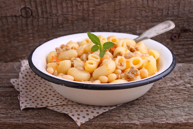 Pasta with meat and beans in a white bowl on the old wooden background