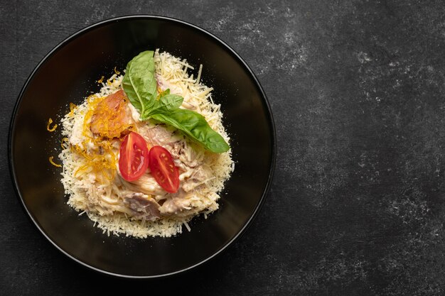 Pasta with meat cheese and basil on a black plate