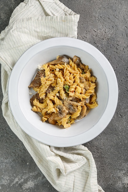 Pasta with mushrooms in white plate on concrete background copy space