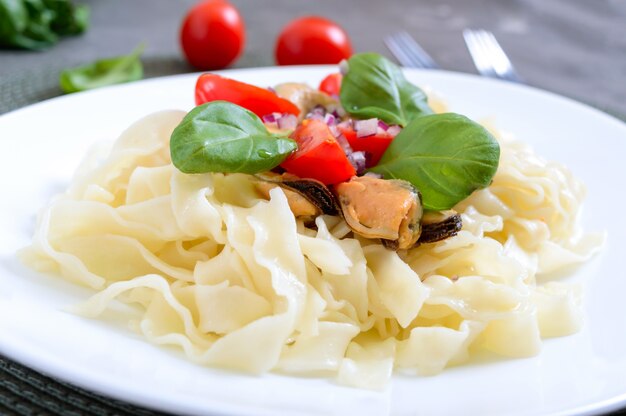 Pasta with mussels, tomatoes on a white plate on a wooden table. Close up