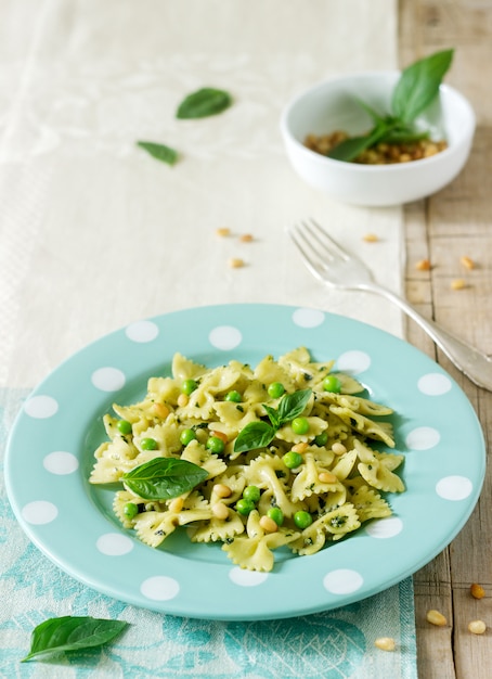 Pasta with pesto sauce, green peas and basil on a wooden table