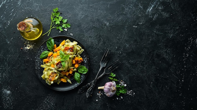 Pasta with pumpkin and spinach in a black plate on a black background Top view Free space for your text