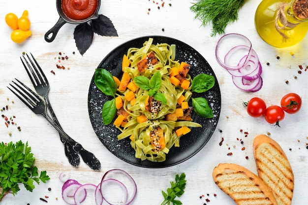 Pasta with pumpkin and spinach in a black plate on a white wooden background Top view Free space for your text