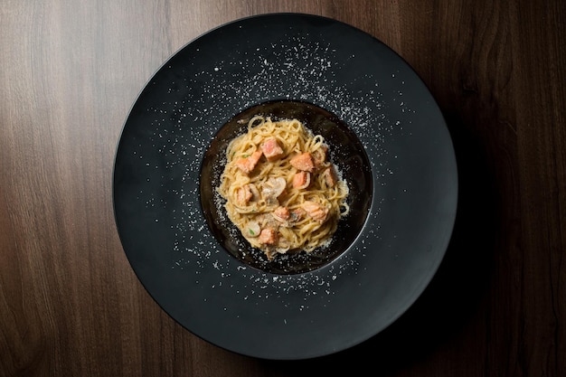 Pasta with salmon fillet mushrooms herbs and egg on a black plate on a wooden background