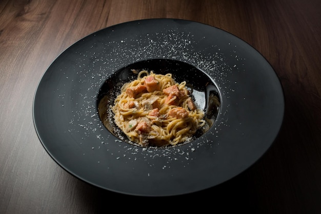 Pasta with salmon fillet mushrooms herbs and egg on a black plate on a wooden background