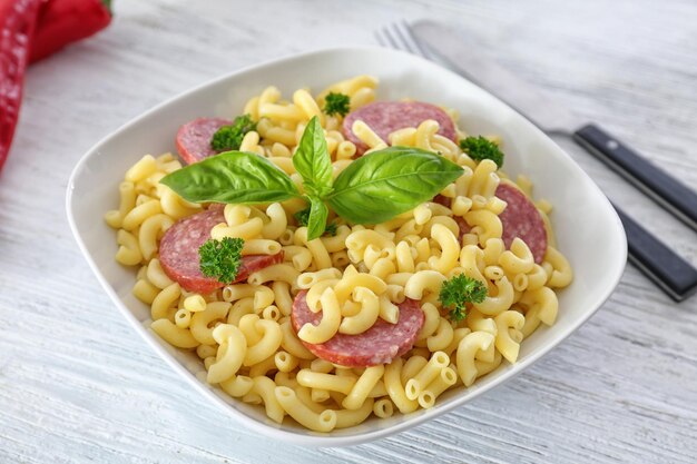 Pasta with sausage in ceramic bowl on light background