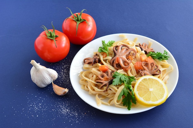 pasta with seafood and tomatoes on the white plate on the dark blue background