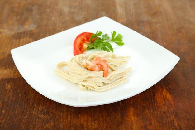 Pasta with shrimps on white plate on wooden background