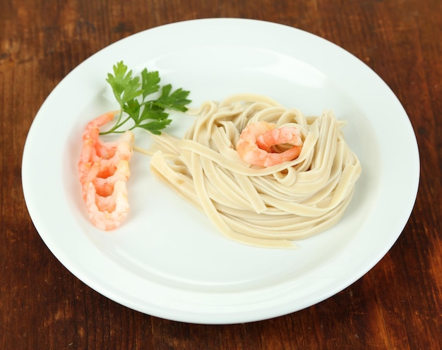 Pasta with shrimps on white plate on wooden background