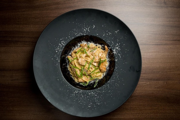 Pasta with slices of chicken parmesan herbs and egg on a black plate on a wooden background