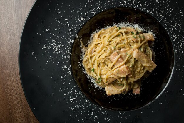 Pasta with slices of ham parmesan cheese herbs and egg on a black plate on a wooden background