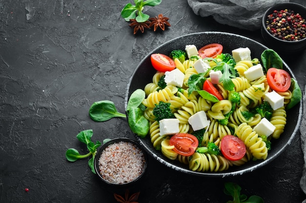 Pasta with spinach tomatoes and feta cheese In a black plate on a wooden background Top view Free space for your text Flat lay