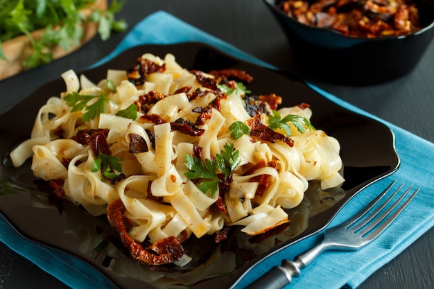 Pasta with sun-dried tomatoes and parsley on a black plate with a blue napkin. greens and sun-dried tomatoes .