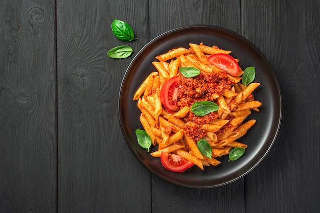 Photo pasta with tomato and meat bolognese sauce and fresh basil on a black background. top view, copy space.