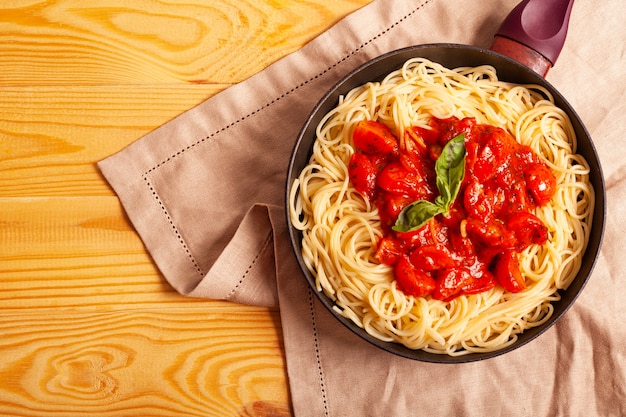 Pasta with tomatoes in a pan on a wooden background