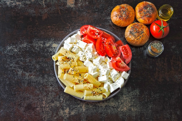 Pasta with tomatoes and white cheese. Vegetarian bowl with pasta, tomatoes and feta. Buns with olive oil. Healthy Italian style food.