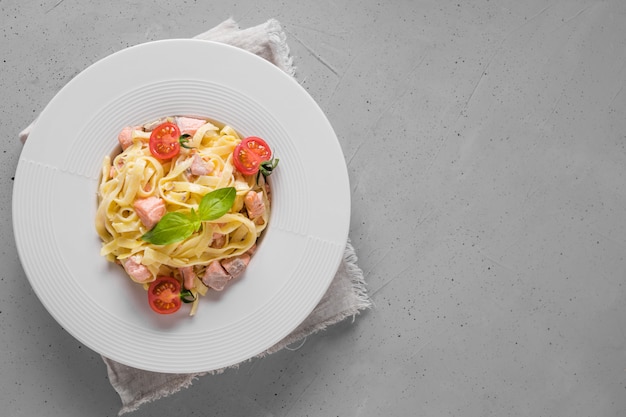 Pasta with trout and tomato in white plate on light. Delicious Mediterranean lunch.